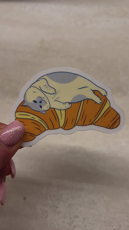 Waterproof and tear-resistant sticker: Adorable cat lounging on a croissant. Ideal for laptops, notebooks, and more—whimsical and durable feline-inspired decal.